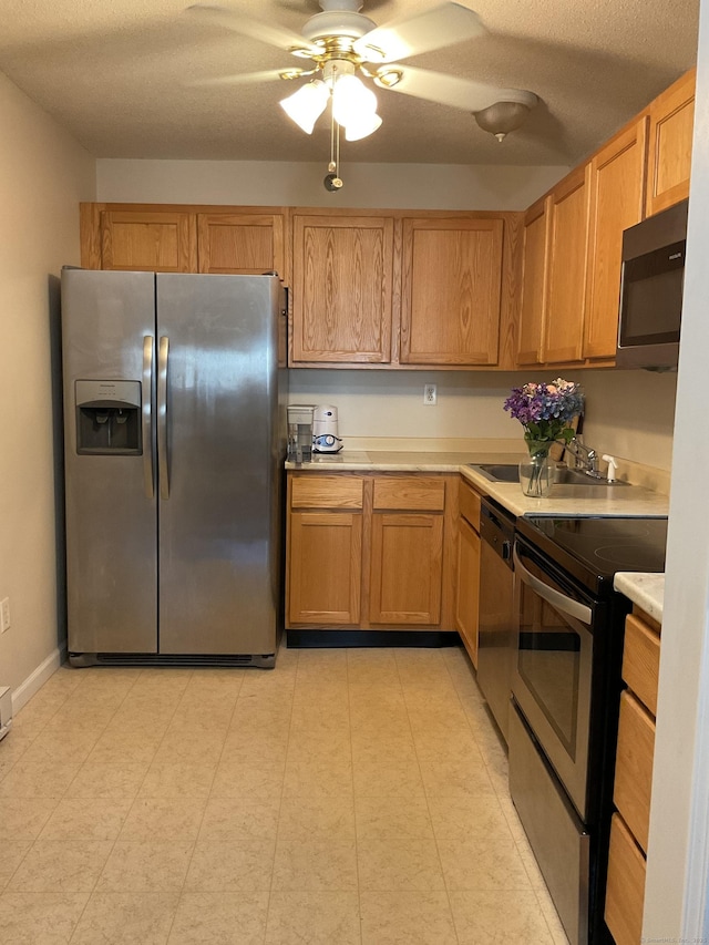 kitchen featuring a ceiling fan, a sink, appliances with stainless steel finishes, light countertops, and baseboards