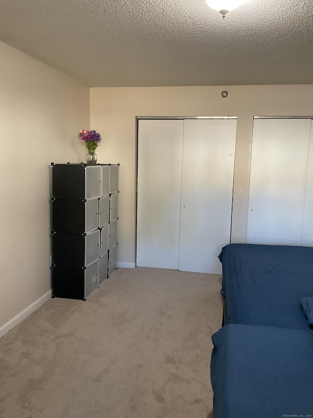 interior space featuring two closets, baseboards, carpet, and a textured ceiling