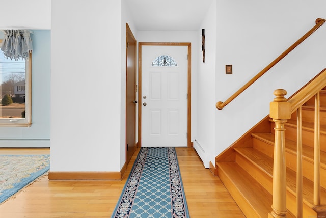 foyer featuring light wood finished floors, stairs, baseboards, and a baseboard radiator