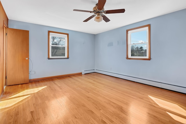 spare room featuring a baseboard heating unit, baseboards, light wood-style flooring, and a ceiling fan