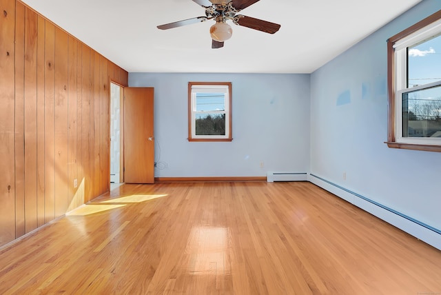 spare room featuring baseboards, light wood-type flooring, wood walls, and a baseboard radiator