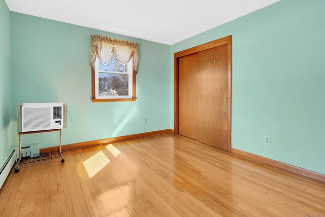 unfurnished bedroom with a closet, a wall mounted air conditioner, baseboards, and wood finished floors