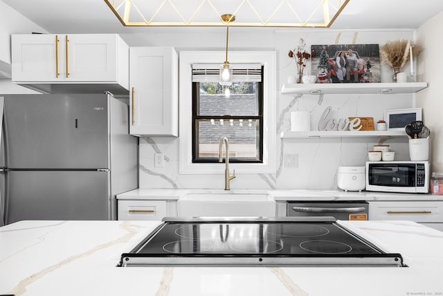 kitchen featuring light stone countertops, decorative backsplash, appliances with stainless steel finishes, white cabinetry, and a sink