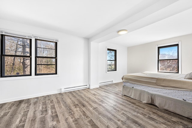 unfurnished bedroom with a baseboard heating unit, multiple windows, and wood finished floors