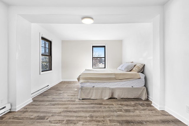 bedroom with baseboards, baseboard heating, and wood finished floors