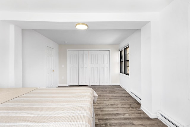 unfurnished bedroom with a closet, a baseboard heating unit, baseboards, and wood finished floors