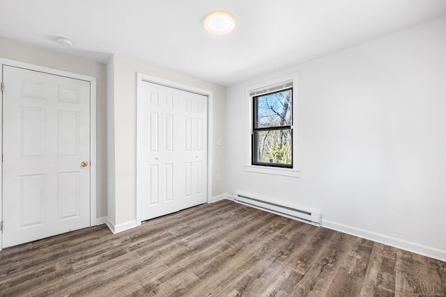 unfurnished bedroom with a closet, baseboards, baseboard heating, and wood finished floors