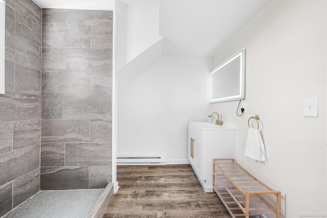 full bathroom featuring a baseboard radiator, wood finished floors, vanity, and a tile shower