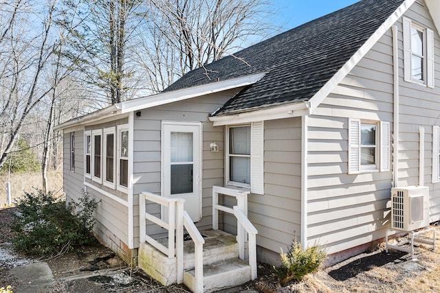 doorway to property with ac unit and a shingled roof