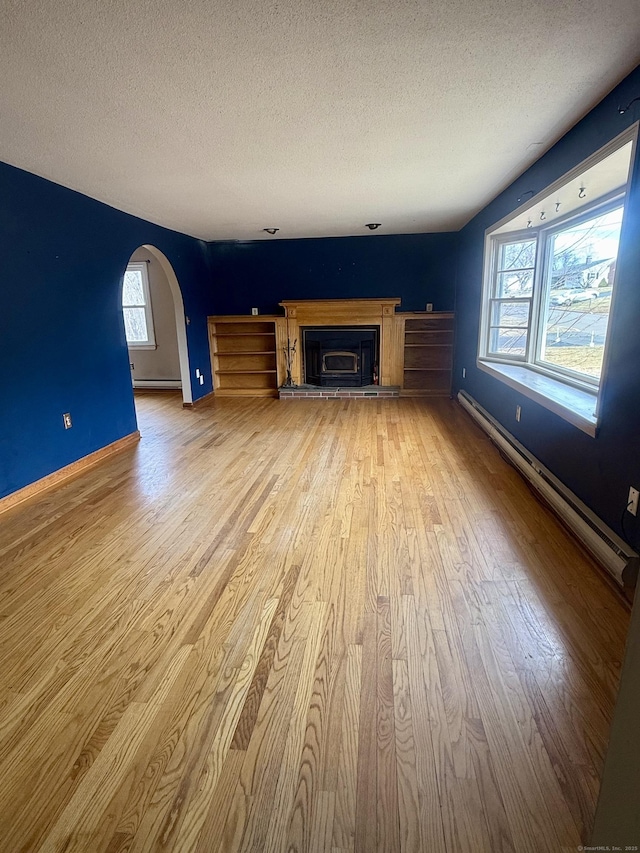 unfurnished living room featuring a baseboard heating unit, arched walkways, a textured ceiling, and light wood-style flooring