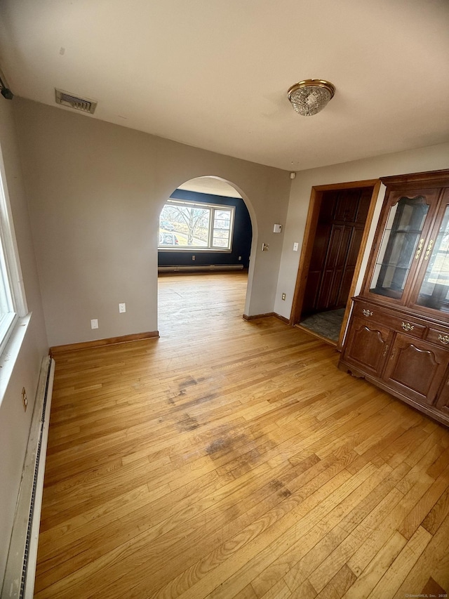 interior space featuring arched walkways, visible vents, light wood-style flooring, and a baseboard radiator