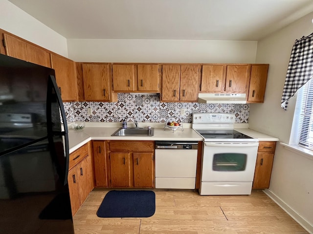 kitchen with tasteful backsplash, under cabinet range hood, light countertops, white appliances, and a sink