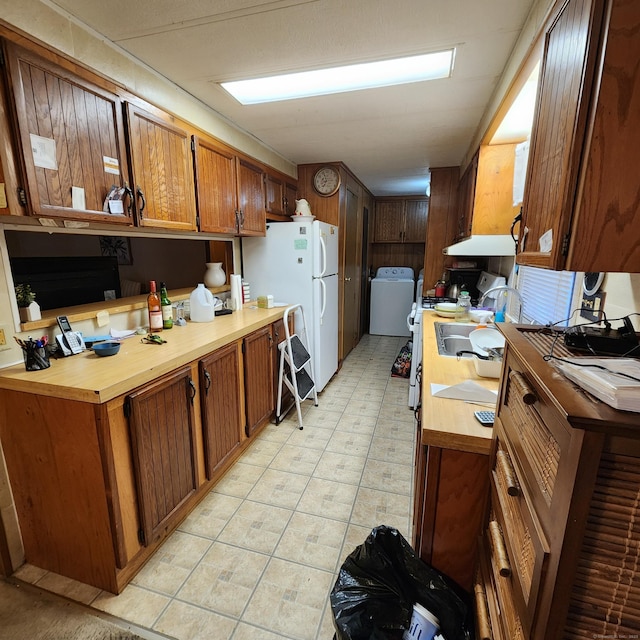 kitchen with under cabinet range hood, washer / dryer, freestanding refrigerator, brown cabinetry, and a sink