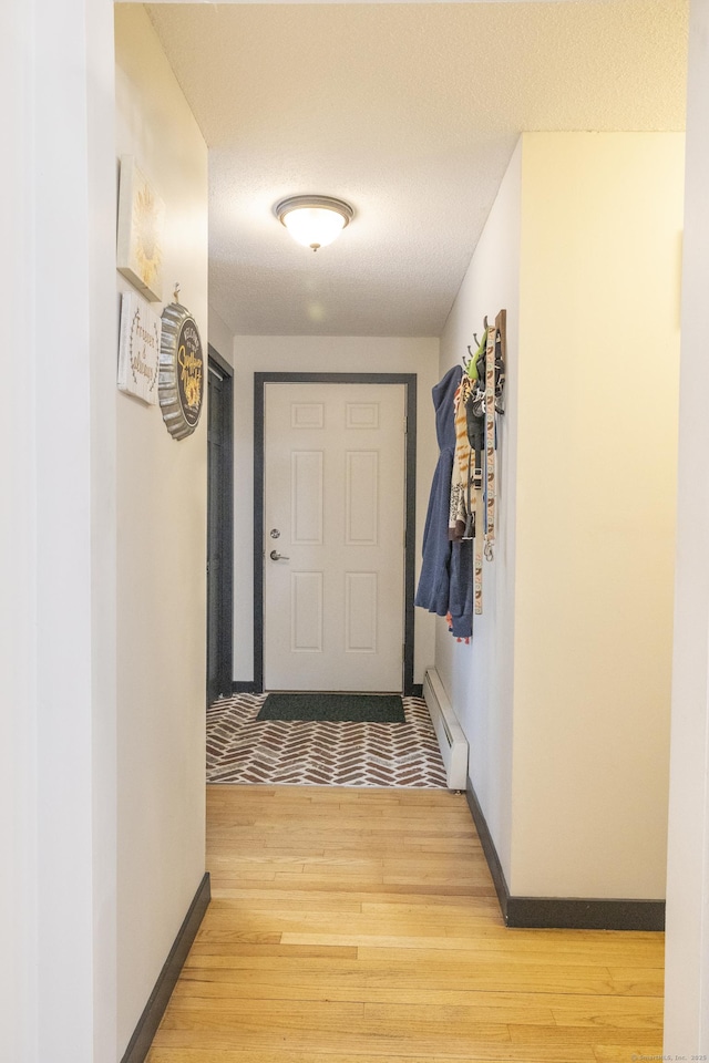 entryway featuring light wood-type flooring, baseboards, baseboard heating, and a textured ceiling