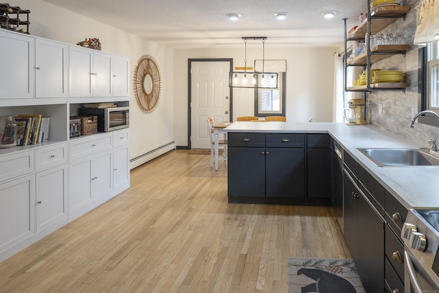 kitchen with a baseboard radiator, appliances with stainless steel finishes, a peninsula, white cabinetry, and a sink