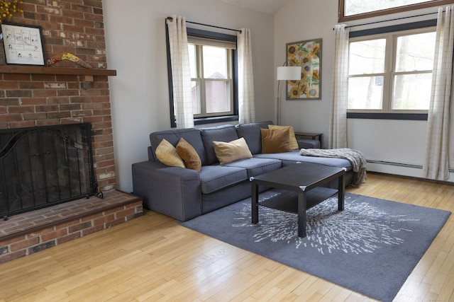 living area with hardwood / wood-style floors, vaulted ceiling, a brick fireplace, and a baseboard heating unit