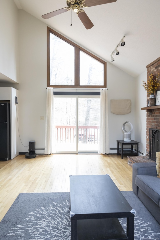 living area featuring high vaulted ceiling, track lighting, wood finished floors, a fireplace, and baseboard heating