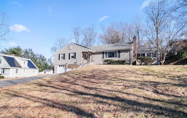 view of front facade with a front lawn, a garage, driveway, and a chimney