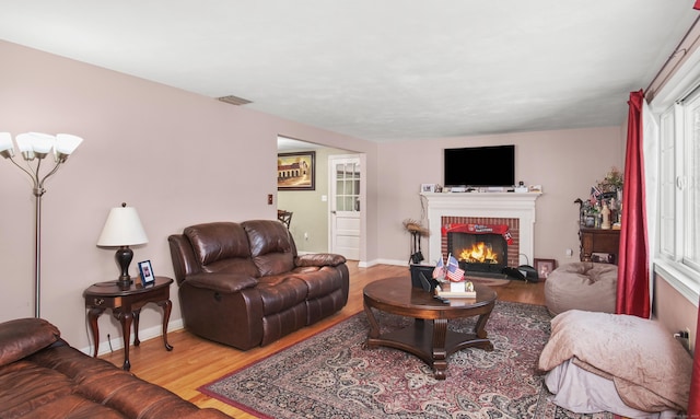 living room with visible vents, baseboards, wood finished floors, and a fireplace