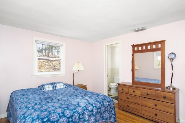 bedroom featuring visible vents, multiple windows, ensuite bath, and wood finished floors