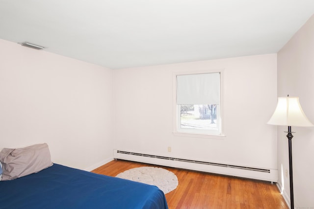 bedroom featuring light wood finished floors, baseboard heating, and visible vents