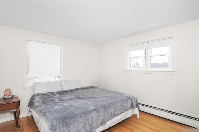 bedroom featuring a baseboard heating unit, baseboards, and wood finished floors