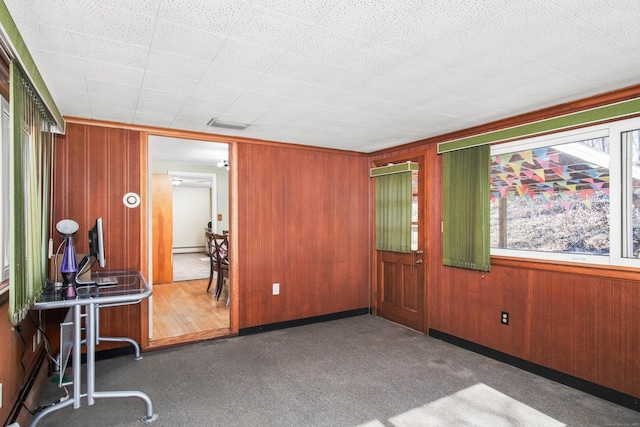 empty room with wooden walls, a baseboard heating unit, and carpet floors