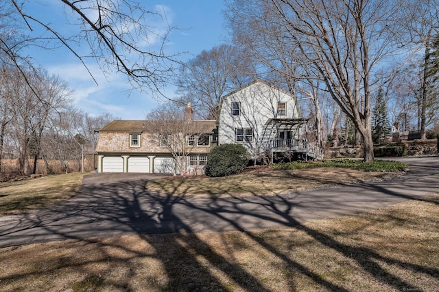 view of front facade with a front yard, driveway, a chimney, stairs, and a garage