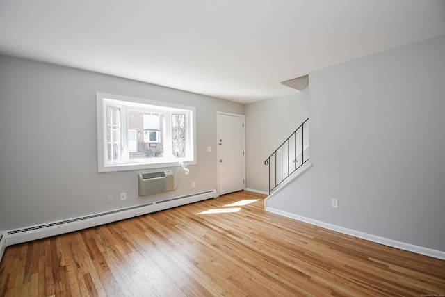 unfurnished room featuring stairway, baseboards, a baseboard radiator, wood-type flooring, and a wall mounted air conditioner