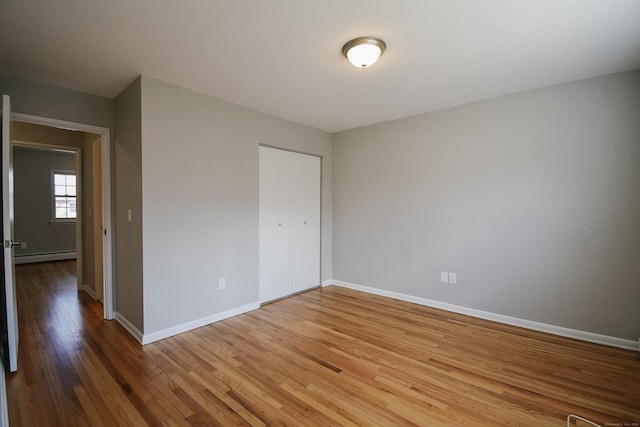 unfurnished bedroom featuring a baseboard heating unit, baseboards, a closet, and wood finished floors