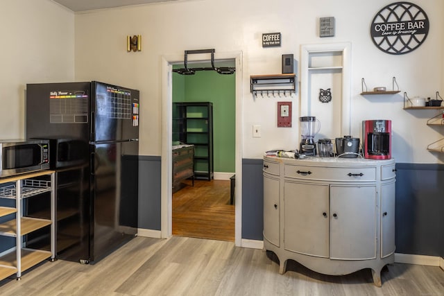 kitchen featuring light wood-type flooring, stainless steel microwave, freestanding refrigerator, light countertops, and baseboards