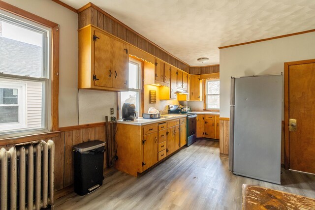 kitchen featuring radiator, a wainscoted wall, stainless steel appliances, light countertops, and wood walls