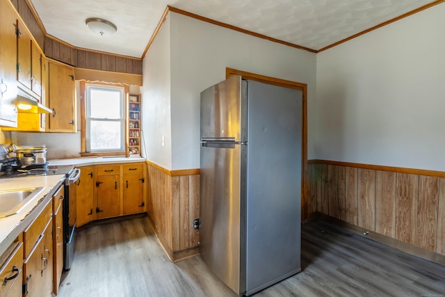 kitchen with wooden walls, stainless steel appliances, light countertops, light wood-style floors, and wainscoting