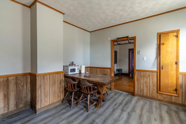 dining area with ornamental molding, a textured ceiling, wood finished floors, wooden walls, and wainscoting