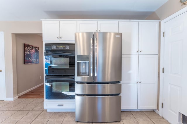 kitchen with dobule oven black, stainless steel refrigerator with ice dispenser, white cabinetry, light tile patterned flooring, and baseboards