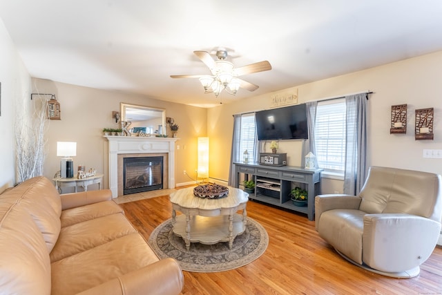 living room with a baseboard heating unit, a fireplace with flush hearth, light wood-style floors, and ceiling fan