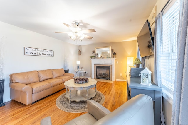 living room featuring a fireplace with flush hearth, ceiling fan, light wood-type flooring, and baseboards