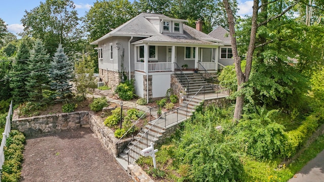 view of front facade featuring stairway, covered porch, and a chimney