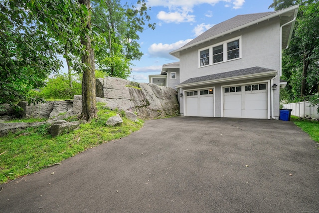 exterior space featuring stucco siding, driveway, fence, an attached garage, and a shingled roof