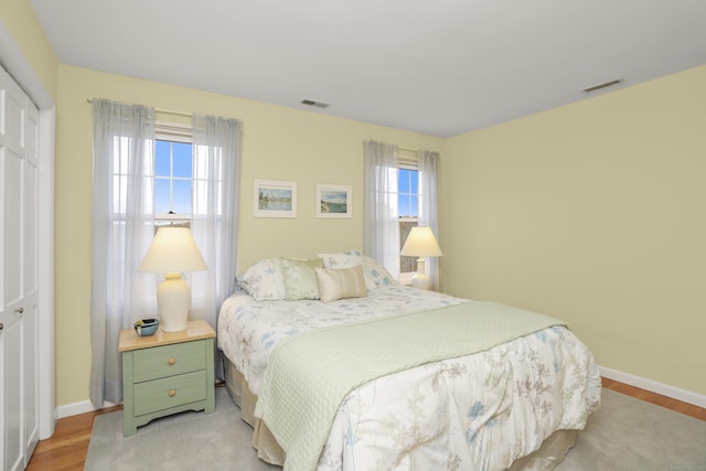 bedroom with a closet, baseboards, visible vents, and light wood finished floors