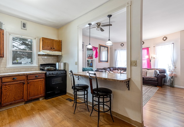 kitchen featuring under cabinet range hood, brown cabinets, light wood-style floors, and black range with gas stovetop