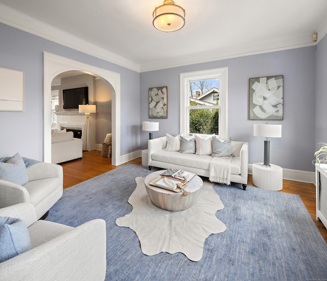 living area featuring arched walkways, ornamental molding, baseboards, and wood finished floors