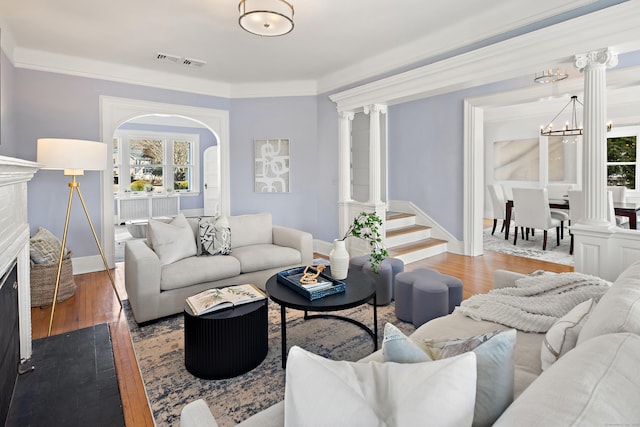 living room featuring visible vents, wood finished floors, a fireplace, and decorative columns