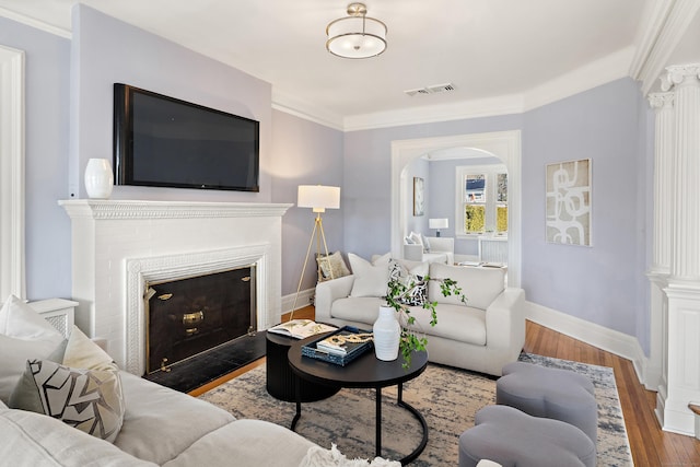 living area featuring visible vents, baseboards, ornamental molding, wood finished floors, and arched walkways