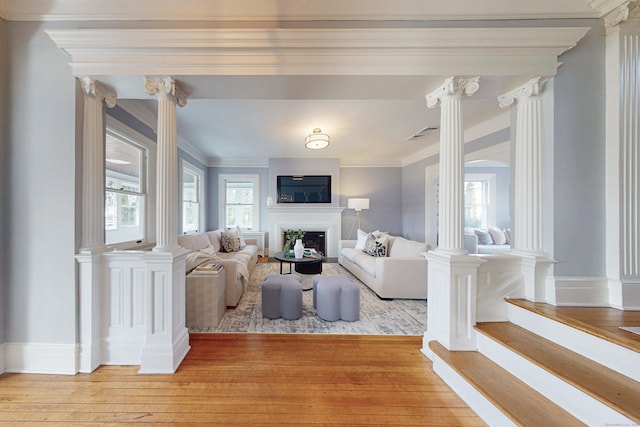 living room featuring decorative columns, crown molding, a fireplace, and light wood finished floors