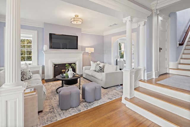 living room featuring crown molding, stairway, visible vents, and ornate columns