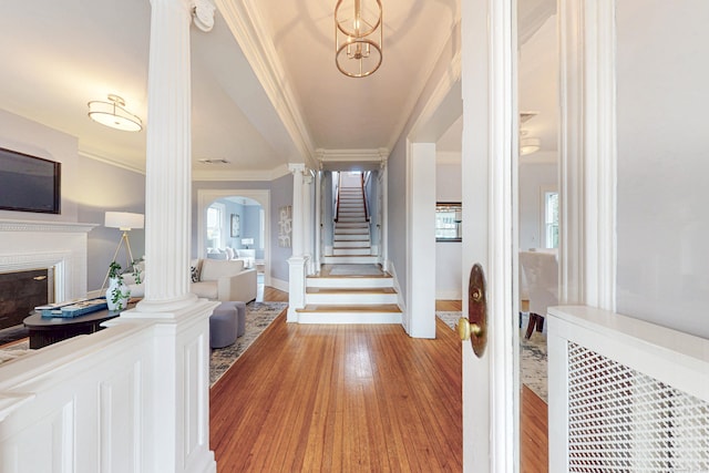 entryway featuring stairway, wood finished floors, decorative columns, a glass covered fireplace, and crown molding