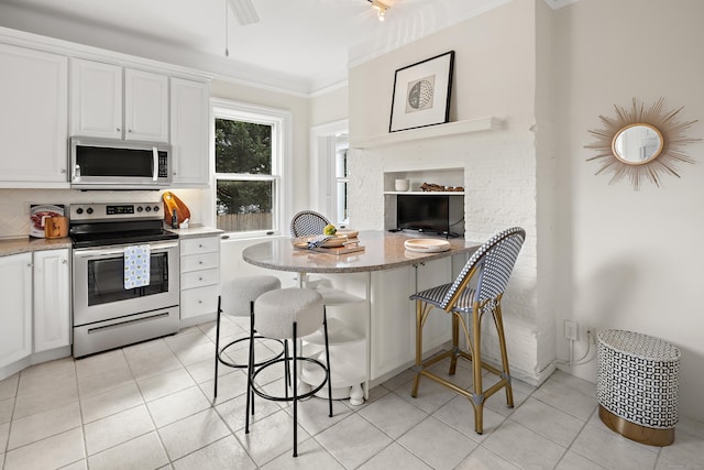 kitchen featuring backsplash, light stone counters, stainless steel appliances, light tile patterned flooring, and white cabinetry