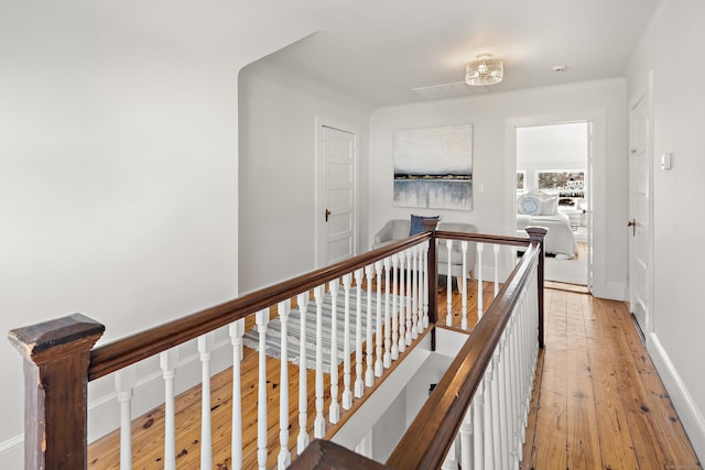 hall with baseboards, an upstairs landing, and light wood-style floors