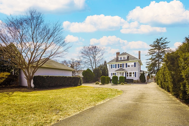 shingle-style home with a front yard, a chimney, and driveway